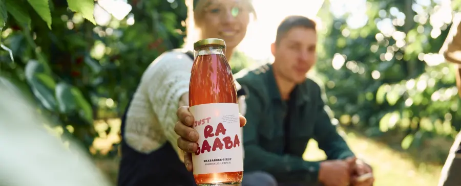 Franzi und Chris Bauer im Obstgarten mit einer Flasche Rhabarber-Sirup