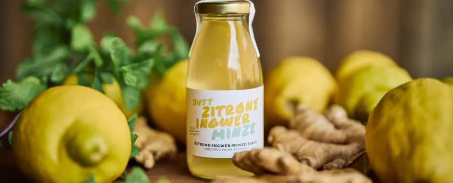 Flasche Zitrone-Ingwer-Minze-Sirup zwischen Zitronen und Ingwer